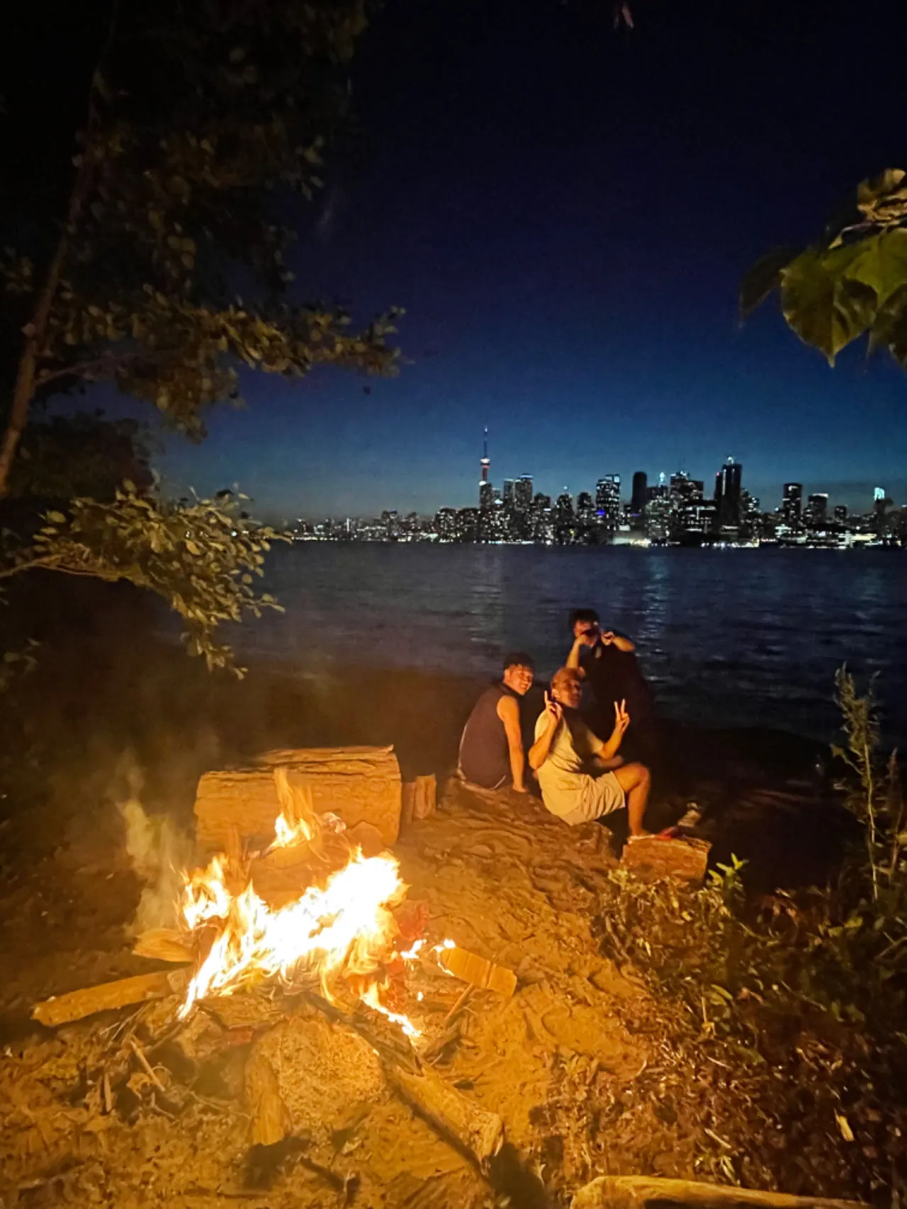 A campfire on the shore with the city skyline behind