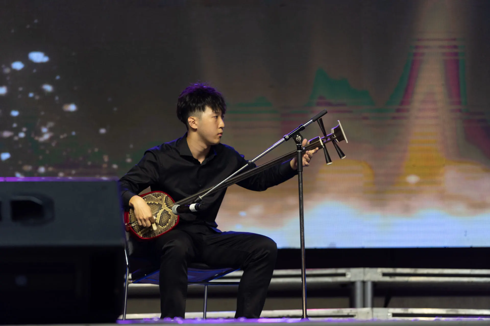 Hongda playing the sanxian on stage under stage lights