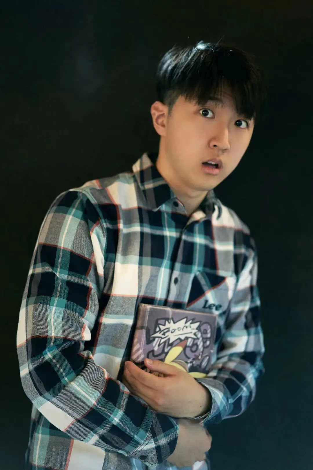 Hongda in a plaid shirt, in character, holding a book