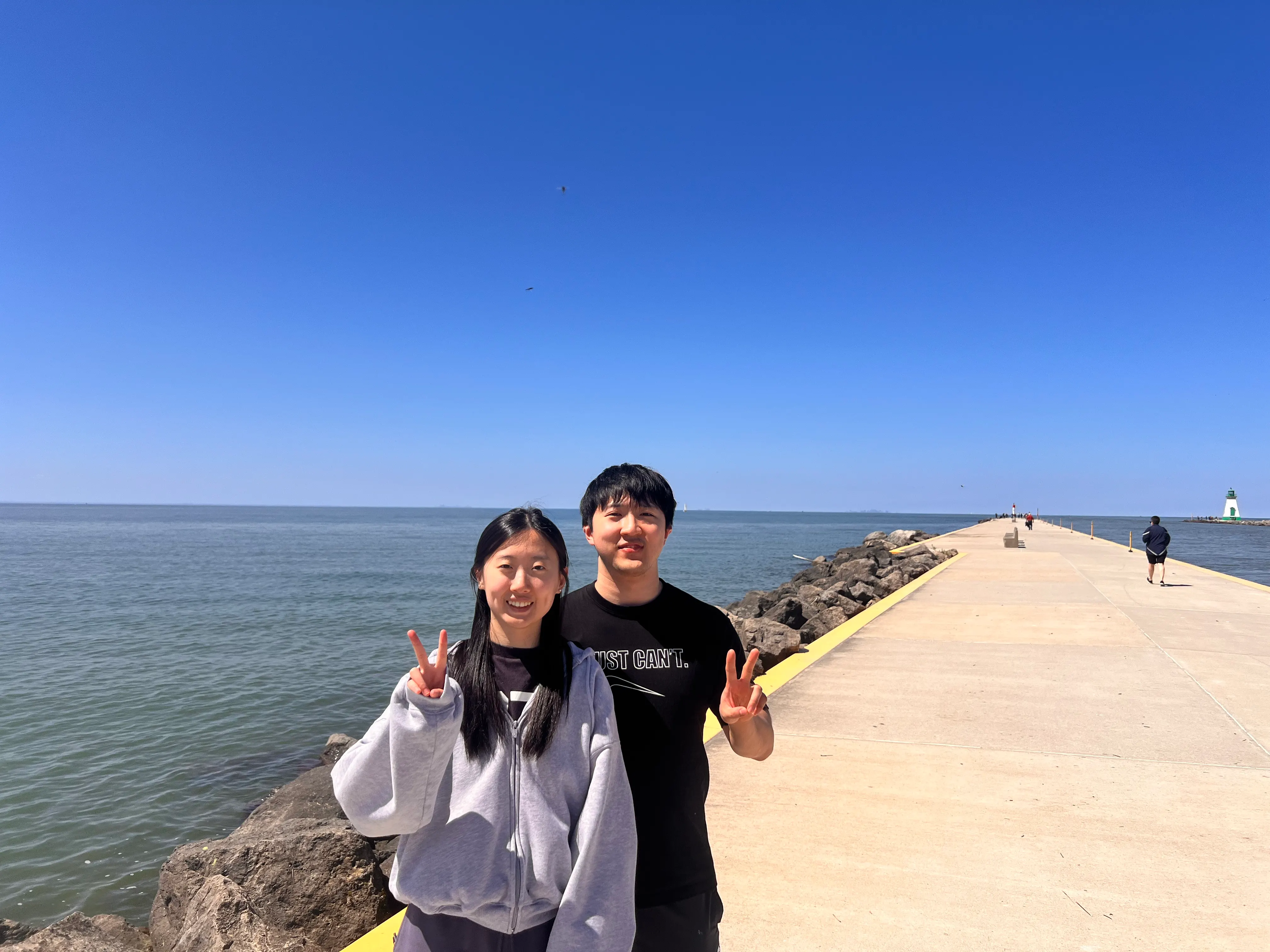 Two people on a breakwater under a clear blue sky