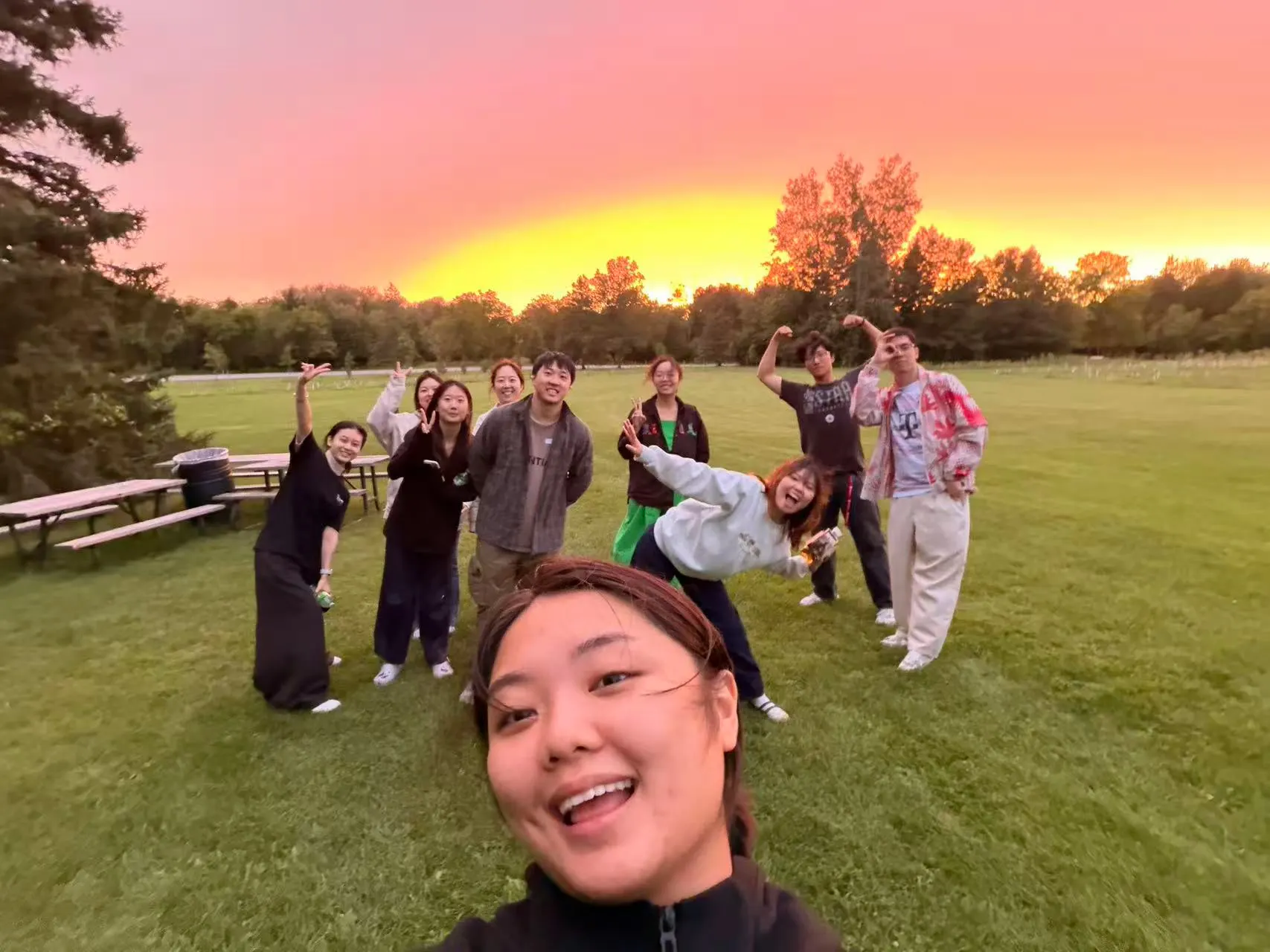 Friends posing on a grassy field under a pink and orange sunset